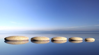 Zen stones row from large to small  in water with blue sky and peaceful landscape background.
