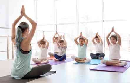 Little children and their teacher practicing yoga in gym